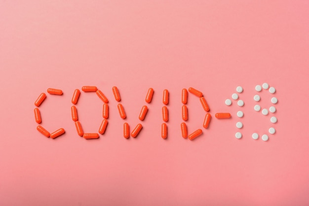 COVID 19 flu epidemic. The inscription Covid-19 of tablets, medicines on a pink background, Flat lay, copy space