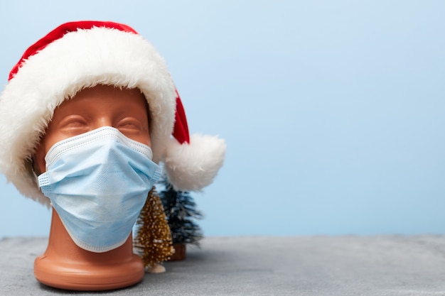 Covid 19, medical mask on a mannequin and christmas hat 2021 on blue background