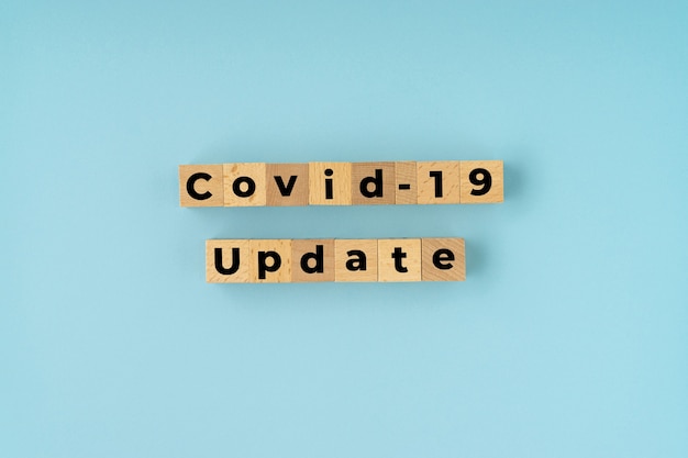 COVID-19 UPDATE text on wooden block with blue Corona virus concept.