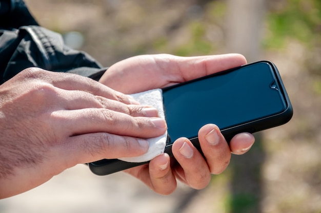 COVID-19. Young Man Outdoors Disinfects Phone Antibacterial Napkin.