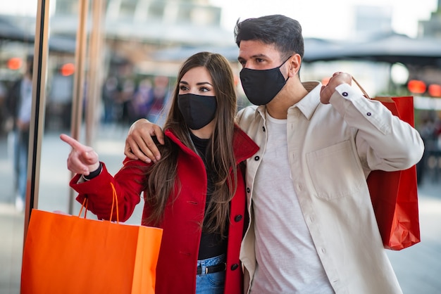 Covid and coronavirus shopping, young couple walking in a city while carrying shopping bags