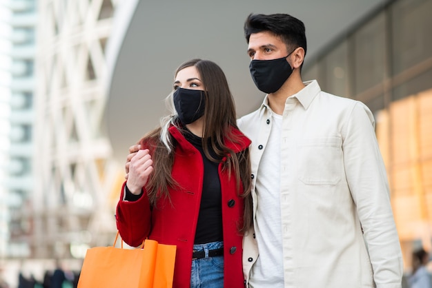 Covid and coronavirus shopping, young couple walking in a city while carrying shopping bags