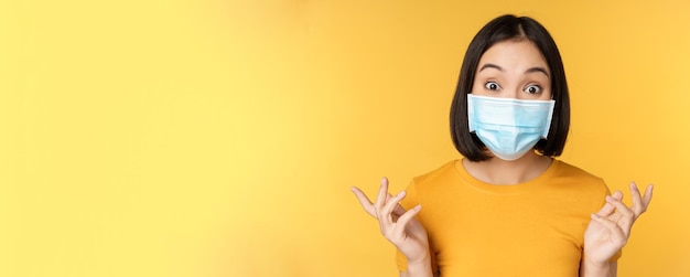 Covid and medical concept close up portrait of asian woman in face mask looking surprised and amazed