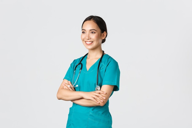 Covid19 healthcare workers pandemic concept Side view of professional confident and hopeful asian female doctor nurse looking assured away and smiling standing in scrubs white background