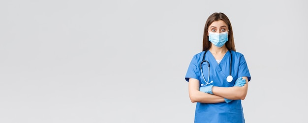 Covid19 preventing virus health healthcare workers and quarantine concept Amused female doctor or nurse in blue scrubs with stethoscope and personal protective equipment look intrigued