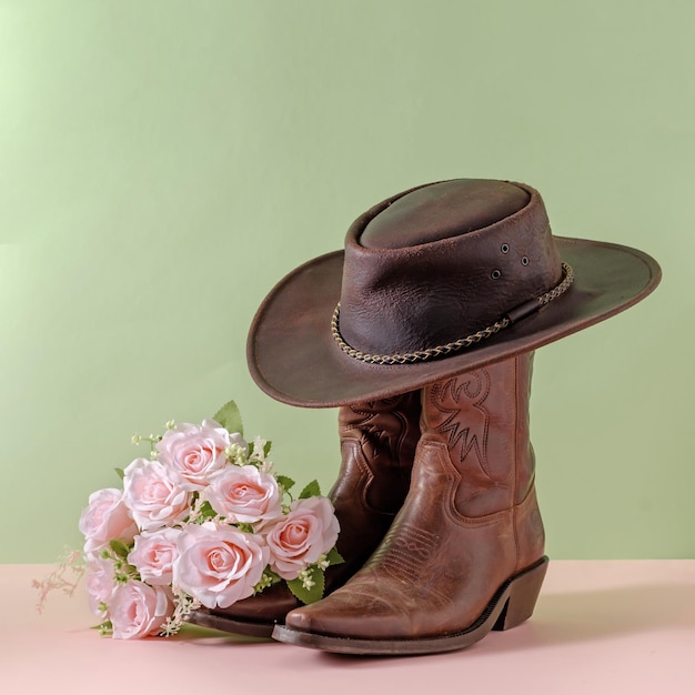 Cowboy boots shoes and hat and bouquet of rose flowers on green background minimal creative concept symbol of wild west america usa texas farm and party