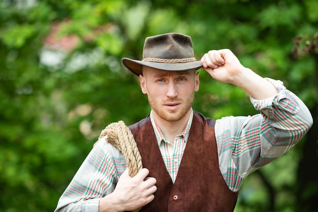 Cowboy farmer man in country side wearing western cowboy hat cowboy with lasso rope on green backgro