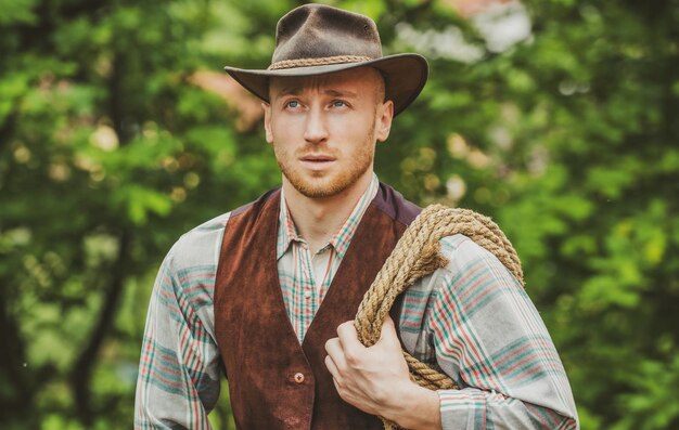 Cowboy with lasso rope on green background western life handsome bearded west farmer portrait of man