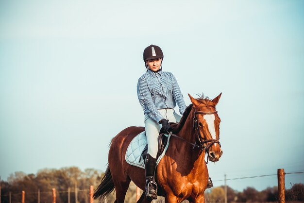 Cowgirl in a hat standing near a horse in a field