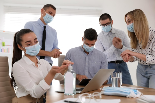 Coworkers with protective masks using hand sanitizer in office Business meeting during COVID19 pandemic