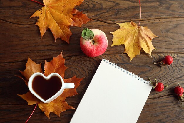 Cozy autumn tea party a cup of tea in the shape of a heart next to a notepad maple leaves apples top view space for text