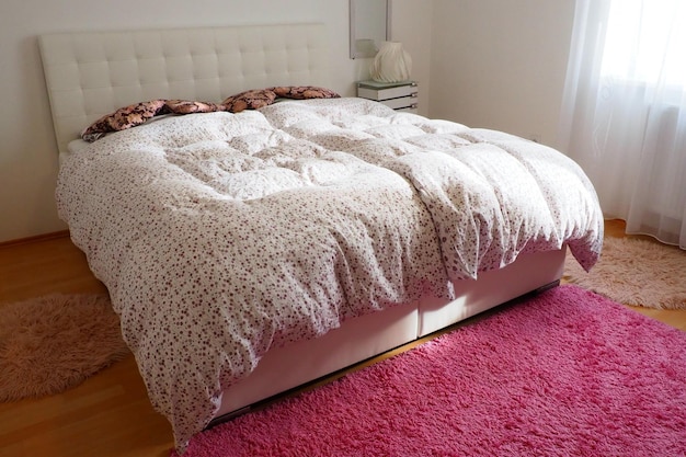 Cozy compact bedroom with white furniture pink carpet and tulle curtains Fluffy feather blanket is thrown over the bed Romantic morning Double double bed with upholstered headboard and upholstery