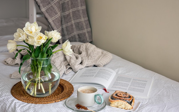 Cozy composition with a bouquet of flowers coffee and a bun in bed