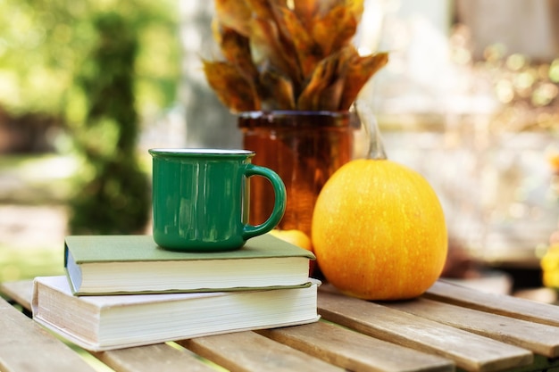 cozy composition with cup of hot tea, stack books and pumpkin on table