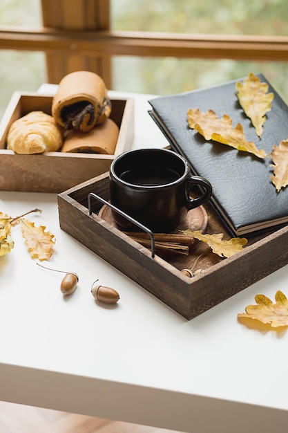 Cozy fall morning at home Coffee cup book and autumn leaves on wooden tray