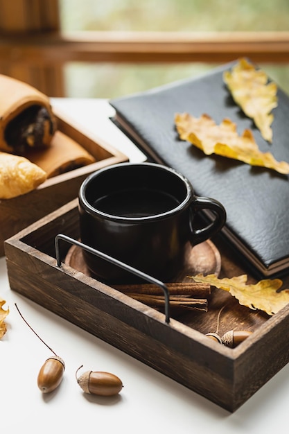 Cozy fall morning at home Coffee cup book and autumn leaves on wooden tray