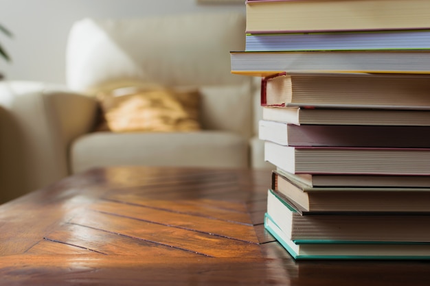 cozy home decoration, white leather couch, wood table and cushions. Pile of books. Reading hobby concept.