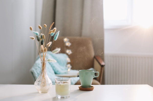 Photo cozy home interior composition with cup of coffee, candle and a vase with flowers on a coffee table