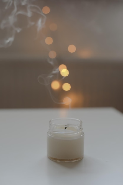 Cozy home interior decor burning candle on table against blurred lights Handmade scented soy wax candle in a glass space for text