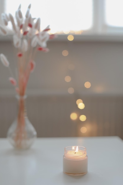 Cozy home interior decor burning candle on table against blurred lights Handmade scented soy wax candle in a glass space for text