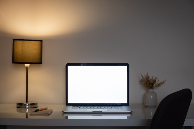 Cozy home office desk at night lit by a lamp and white laptop screen.