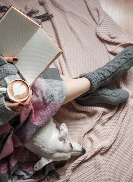 Cozy home woman covered with warm blanket drinks coffee sleeping dog next to woman