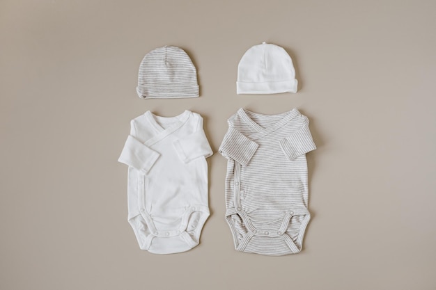 Cozy hygge clothes and accessories for newborn baby Basic bodysuits hats on pastel beige background Aesthetic minimalist baby fashion collage