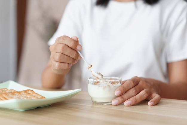 Cozy lifestyle concept Young woman eating yogurt and crackers for snack while relaxation at home