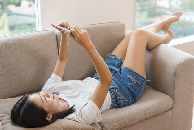 Cozy lifestyle concept Young woman lying on couch and use smartphone to watching movie at home