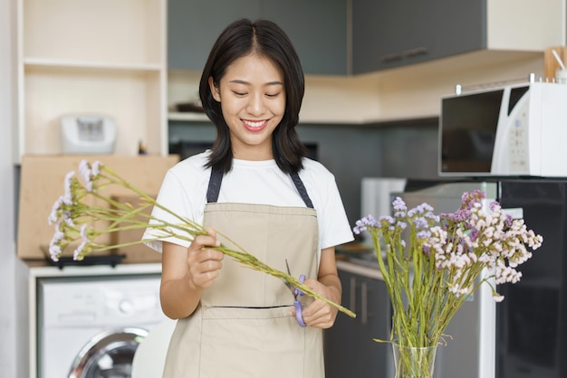 Cozy lifestyle concept Young woman use scissor to trim flowers for arrangement in vase on table