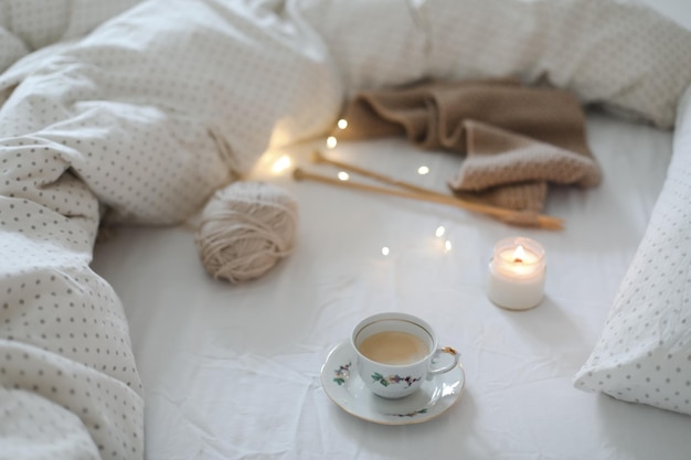 Cozy morning still life with a coffee cup candle needles and a woolen yarn in white bed knitting war