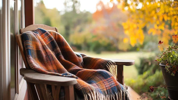 Photo cozy plaid blanket on a wooden rocking chair on a porch with a beautiful autumn view