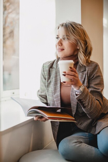 Photo cozy relaxation woman with book and coffee by window leisure time reading with warm drink relax