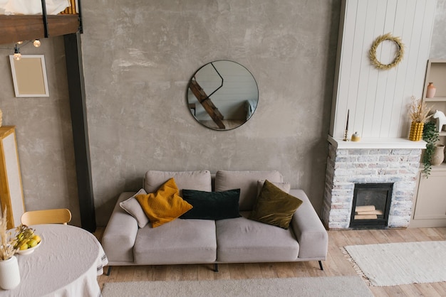 Cozy Scandinavian style interior of a living room with a gray sofa with pillows a round dining table and a fireplace in a country house