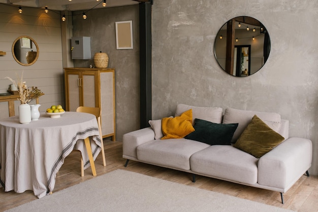 Cozy Scandinavian style interior of the living room with a gray sofa with pillows round dining table