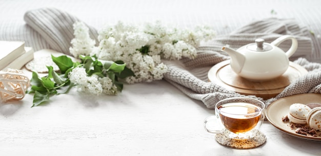 Cozy spring composition with a cup of tea, a teapot, french macaroons, lilac color on a light blurred table.