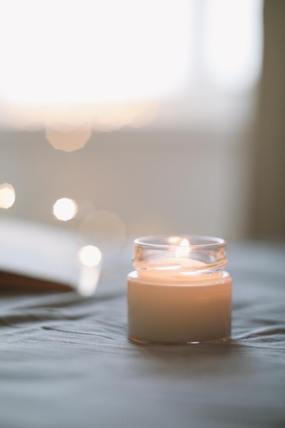 Cozy still life composition with a scented burning candle in glass jar in bed close up Good morning Cozy home