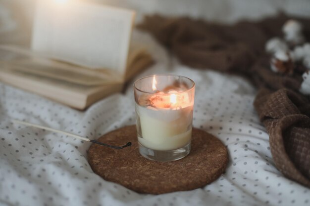 Cozy still life interior details with a book candle and a cotton twig in warm soft bed sweet home