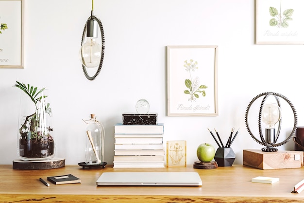 Cozy and stylish composition of creative worskpace interior design with mock up poster frame, wooden desk, lamp, plants and design office accessories. Neutral walls, bright elements. Template.