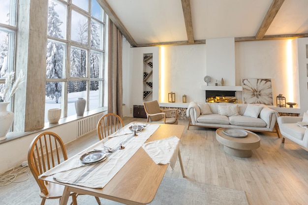 Cozy warm home interior of a chic country chalet with a huge panoramic window overlooking the winter forest open plan wood decoration warm colors and a family hearth