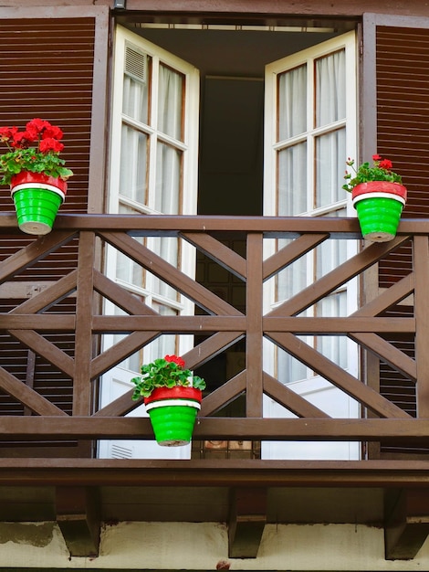 Cozy wooden balcony of dark brown colour with double doors shutters and vibrant pot flowers