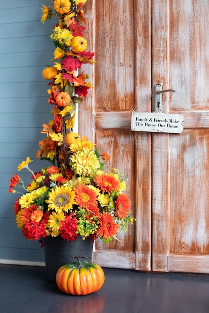 Cozy wooden porch of house with pumpkin, yellow fall leaves and flowers.