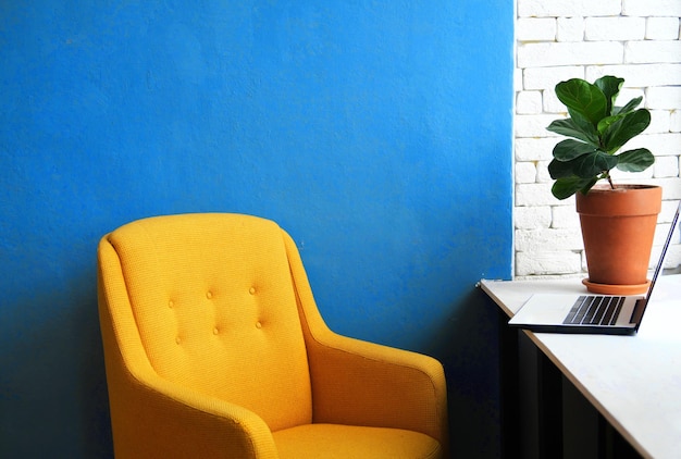 Cozy workplace A stylish yellow armchair stands near the table on which there is a laptop and a pot with a live plant