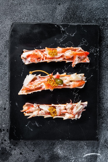 Crab leg meat in a sheel with herbs. Black background. Top view.