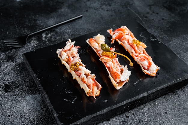 Crab leg meat in a sheel with herbs. Black background. Top view.