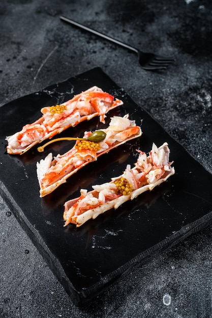 Crab leg meat in a sheel with herbs. Black background. Top view.