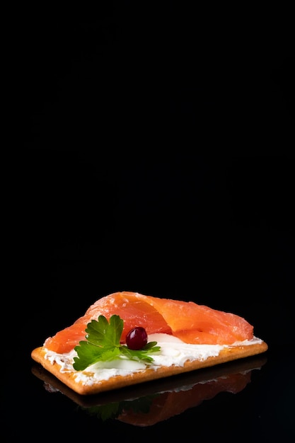 Cracker with curd cheese and salted salmon isolated on black Text space