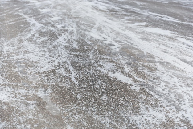 Cracks on the asphalt filled with snow. Low drifting snow on a Winter road texture background