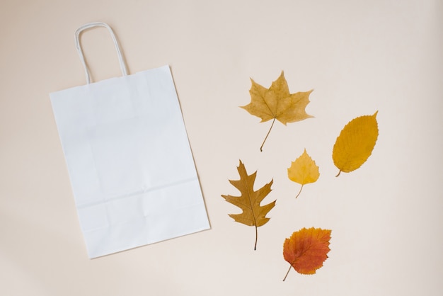 Craft bag white for your purchases with autumn leaves on a background of beige paper. Autumn concept. top view copy space