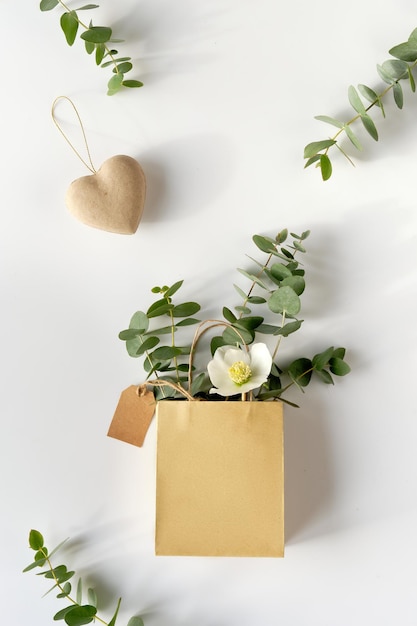 Craft bag with wintertime eucalyptus and white Helleborus flower. Brown paper tag and cardboard heart. Winter flat lay with evergreen twigs.